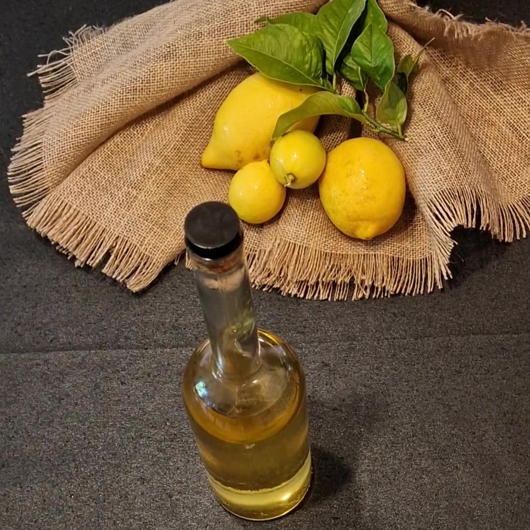 Botellas de limoncello casero color dorado, servidas con rodajas de limón y copas heladas sobre una mesa de madera.