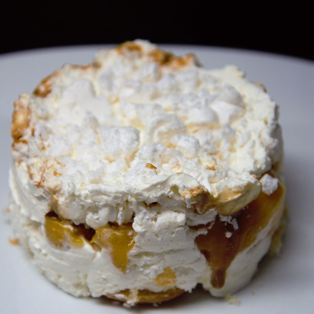 Postre Chajá servido en capas en una copa de cristal: bizcochuelo, dulce de leche, merenguitos desmenuzados, chantilly y trozos de melocotón